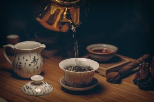asian inspired tea set, with hot water being poured into tea cup with loose leaf in it. 