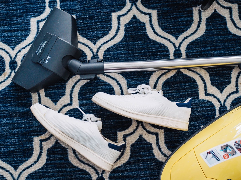 A vacuum being used on a carpet with white shoes on it.